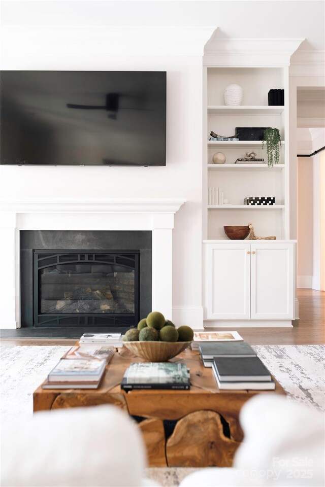 living area featuring built in features, wood finished floors, a glass covered fireplace, and ornamental molding