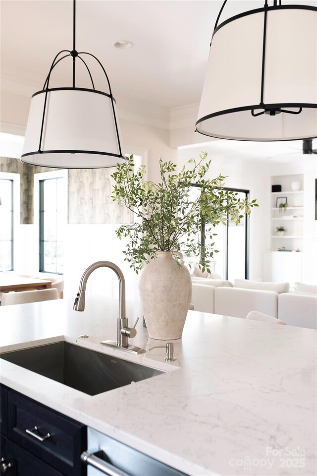 interior space with built in shelves, crown molding, light stone countertops, pendant lighting, and a sink