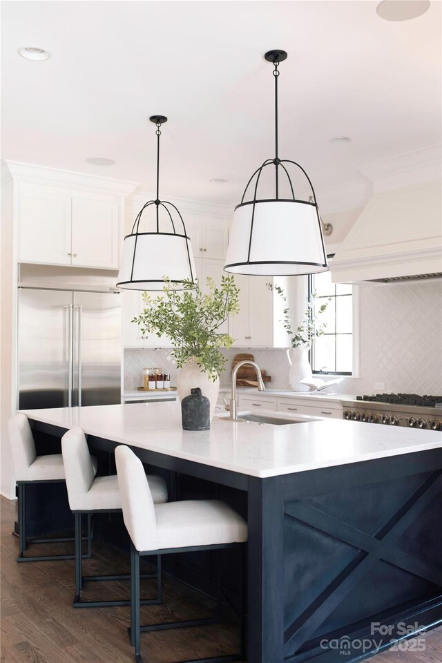 kitchen featuring stainless steel built in fridge, custom range hood, a sink, white cabinetry, and light countertops