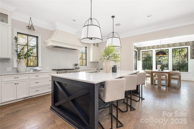 kitchen with hardwood / wood-style flooring, a kitchen breakfast bar, premium range hood, and ornamental molding