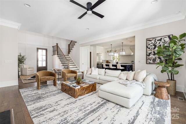 living room with ornamental molding, stairway, baseboards, ceiling fan, and dark wood-style flooring