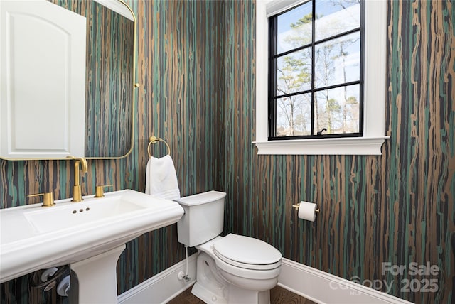 half bath featuring a sink, baseboards, toilet, and wallpapered walls