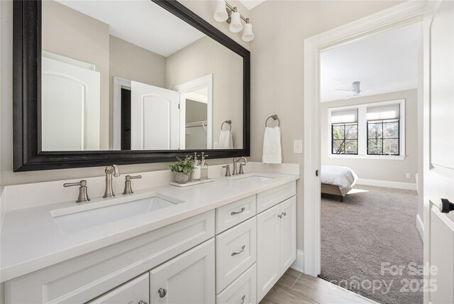 full bathroom with double vanity, connected bathroom, baseboards, and a sink