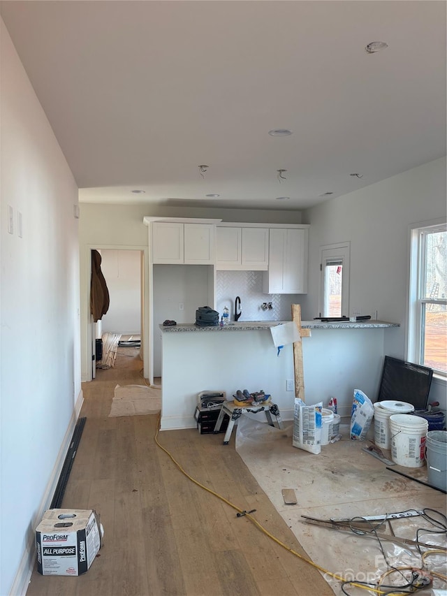 kitchen featuring light wood-type flooring, light stone countertops, white cabinets, and backsplash