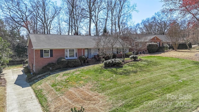 ranch-style home featuring a front yard, fence, brick siding, and a shingled roof