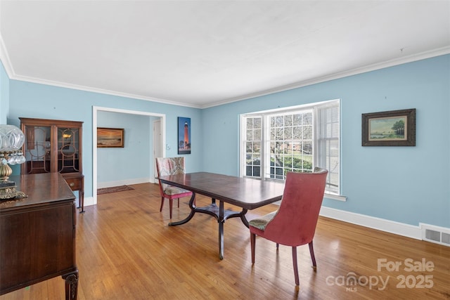 dining room with visible vents, baseboards, wood finished floors, and crown molding