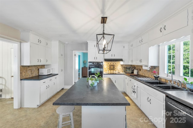 kitchen with dark countertops, under cabinet range hood, white cabinets, black appliances, and a sink