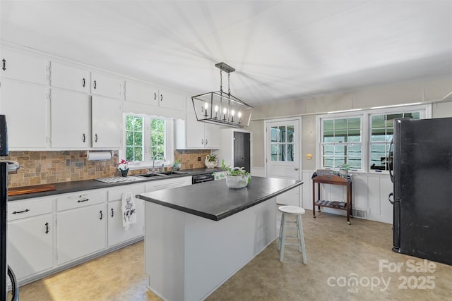 kitchen with dark countertops, tasteful backsplash, white cabinets, black appliances, and a sink