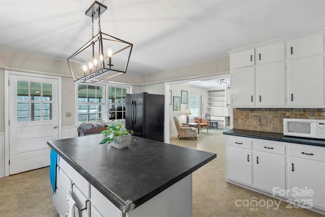 kitchen featuring white microwave, dark countertops, a kitchen island, freestanding refrigerator, and white cabinetry