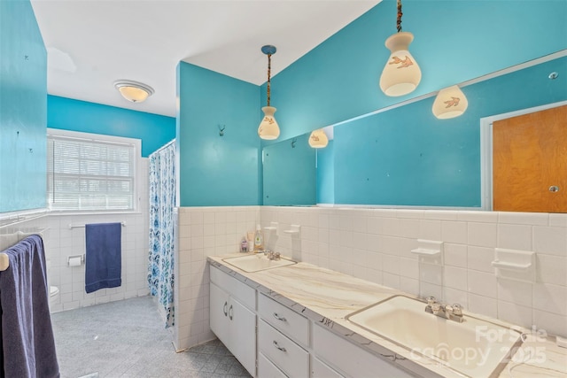 full bath with tile walls, double vanity, wainscoting, and a sink