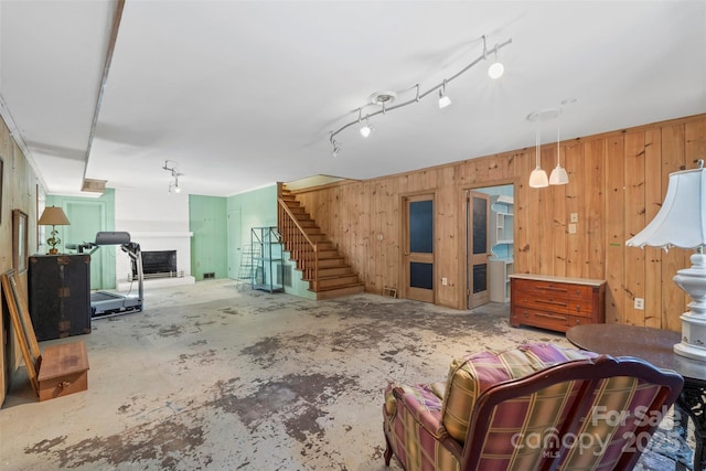 living area with wooden walls, a fireplace with raised hearth, track lighting, concrete flooring, and stairs