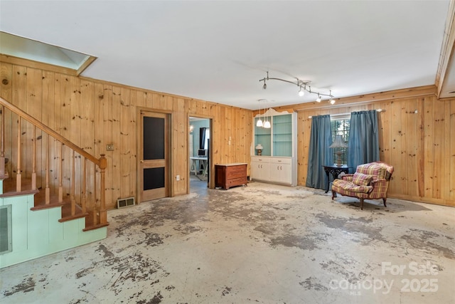 unfurnished living room featuring visible vents, unfinished concrete floors, stairs, and wooden walls