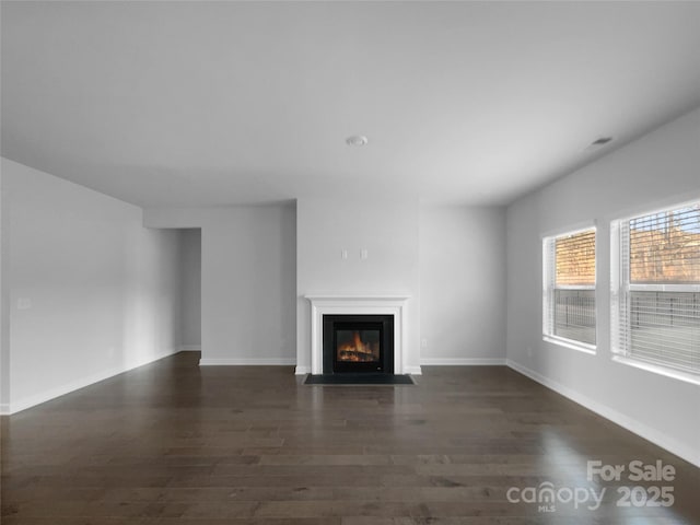 unfurnished living room featuring a fireplace with flush hearth, baseboards, and wood finished floors