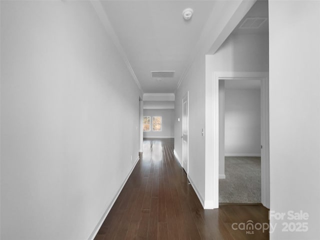 hallway with dark wood-type flooring, visible vents, crown molding, and baseboards