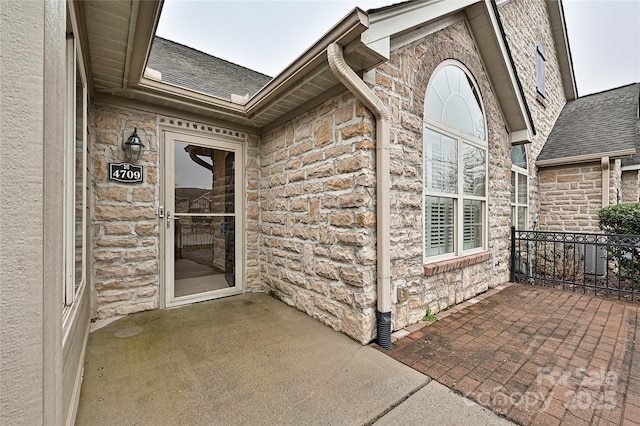 entrance to property featuring stone siding, a shingled roof, and stucco siding