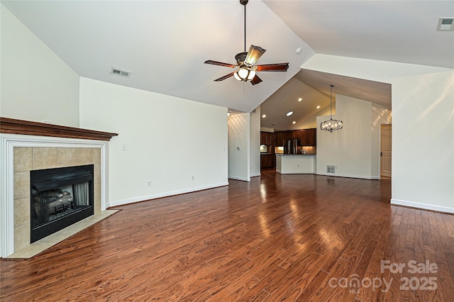 unfurnished living room featuring dark wood-style floors, visible vents, a tiled fireplace, and ceiling fan with notable chandelier