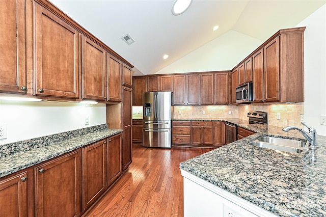 kitchen featuring appliances with stainless steel finishes, dark wood-type flooring, dark stone countertops, and a sink