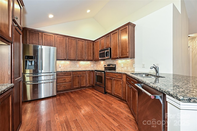 kitchen with dark stone counters, lofted ceiling, appliances with stainless steel finishes, dark wood-style flooring, and a sink