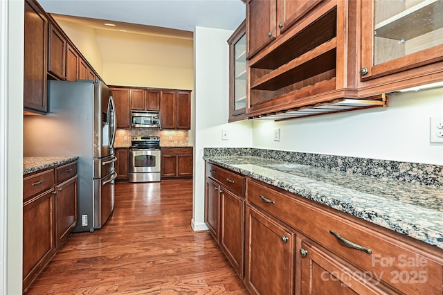 kitchen featuring tasteful backsplash, glass insert cabinets, dark stone countertops, dark wood-type flooring, and stainless steel appliances