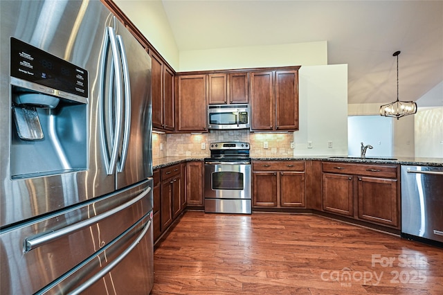 kitchen with lofted ceiling, a sink, dark wood-style floors, appliances with stainless steel finishes, and dark stone counters