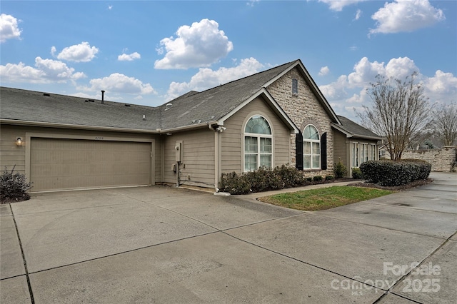 view of front of house featuring stone siding, roof with shingles, an attached garage, and concrete driveway