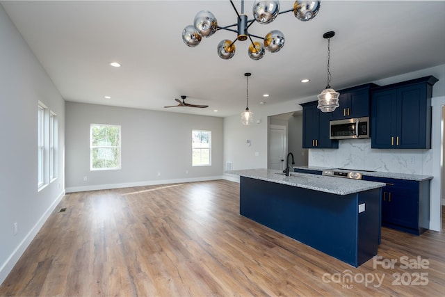 kitchen with decorative backsplash, light wood-style flooring, stainless steel microwave, blue cabinetry, and a sink