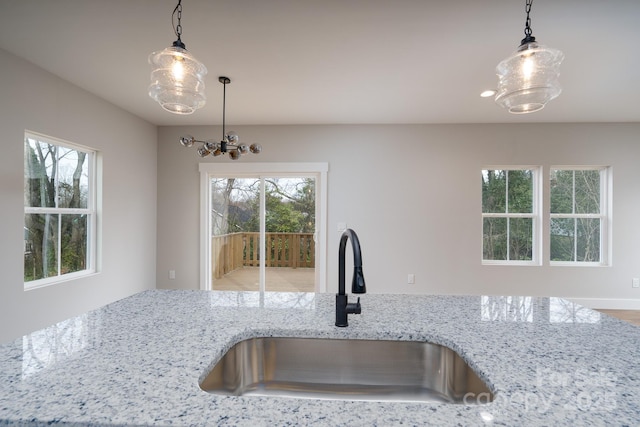 kitchen with a sink, decorative light fixtures, and light stone countertops