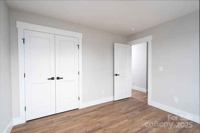 unfurnished bedroom with a closet, wood finished floors, and baseboards