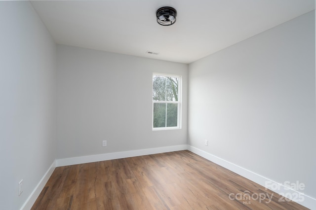 spare room with wood finished floors, visible vents, and baseboards