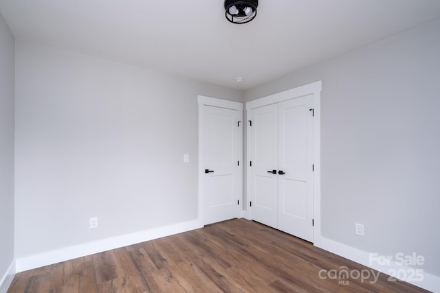 unfurnished bedroom with a closet, wood finished floors, and baseboards