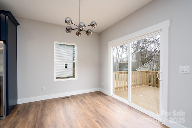 unfurnished dining area with an inviting chandelier, wood finished floors, visible vents, and baseboards