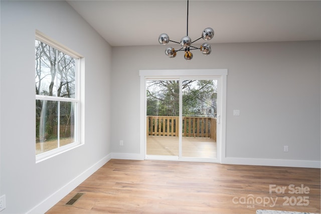 unfurnished dining area with visible vents, light wood finished floors, a wealth of natural light, and an inviting chandelier