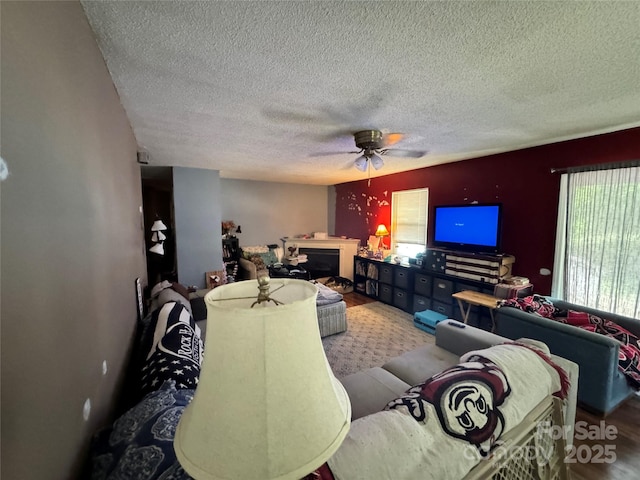 living area with ceiling fan, a textured ceiling, wood finished floors, and a fireplace