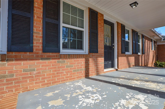 view of exterior entry featuring covered porch and brick siding