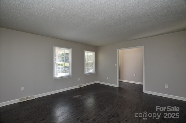 unfurnished room with dark wood-type flooring, visible vents, and baseboards