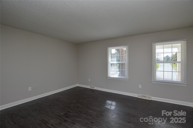 unfurnished room with a textured ceiling, dark wood-type flooring, visible vents, and baseboards