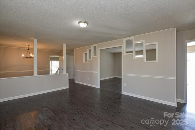 spare room featuring a chandelier, a textured ceiling, dark wood-style flooring, baseboards, and ornate columns