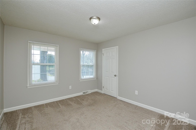 carpeted spare room featuring visible vents, a textured ceiling, and baseboards