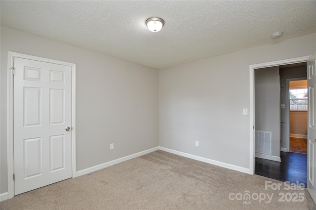 carpeted spare room with a textured ceiling, visible vents, and baseboards