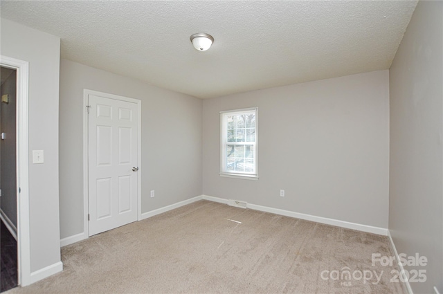 empty room with light carpet, a textured ceiling, visible vents, and baseboards