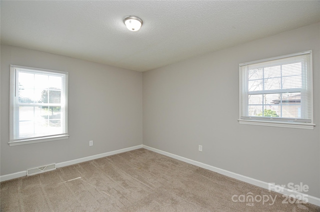 spare room featuring visible vents, light carpet, baseboards, and a textured ceiling