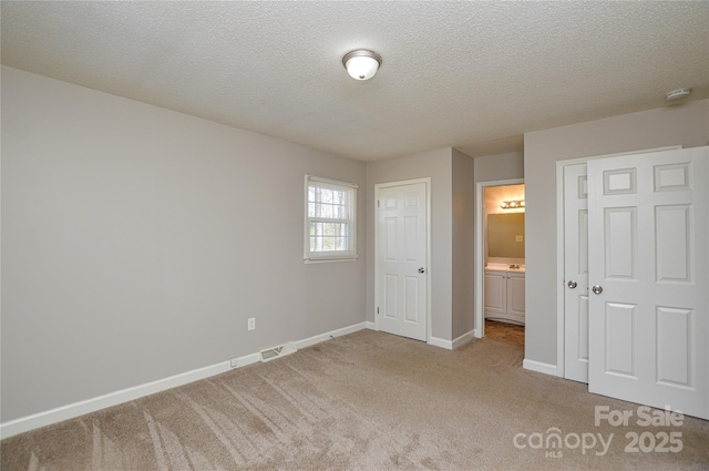 unfurnished bedroom featuring a textured ceiling, ensuite bathroom, visible vents, baseboards, and carpet