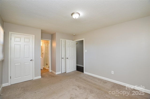 unfurnished bedroom with light colored carpet, ensuite bath, a textured ceiling, and baseboards