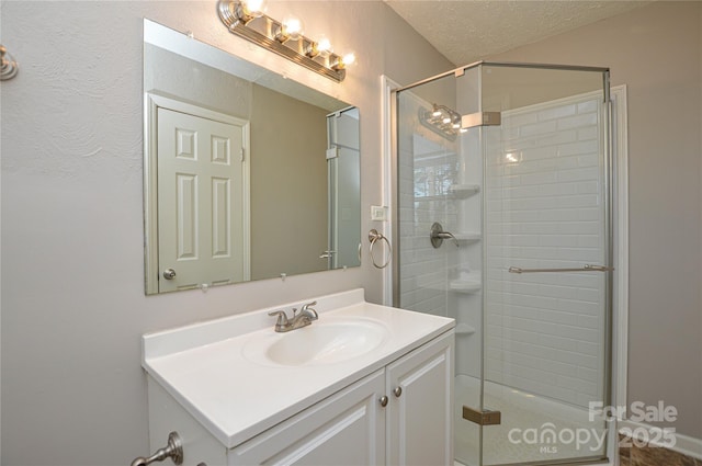 full bathroom featuring a textured ceiling, a shower stall, and vanity