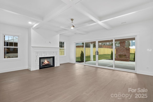 unfurnished living room with wood finished floors, coffered ceiling, beamed ceiling, a lit fireplace, and baseboards