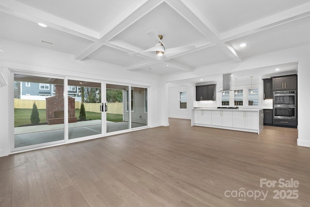 unfurnished living room with a healthy amount of sunlight, beam ceiling, coffered ceiling, and wood finished floors