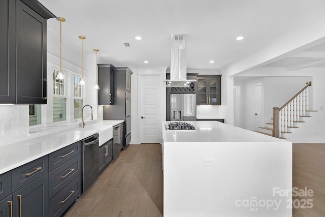 kitchen with a sink, appliances with stainless steel finishes, wood finished floors, and island exhaust hood