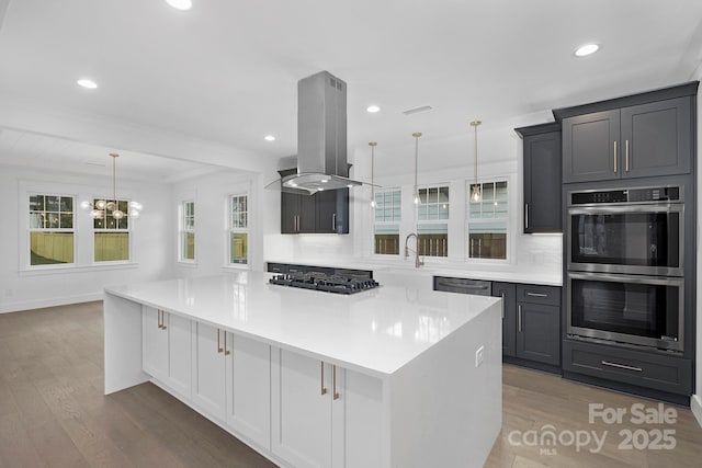 kitchen with island range hood, stainless steel appliances, wood finished floors, light countertops, and a large island