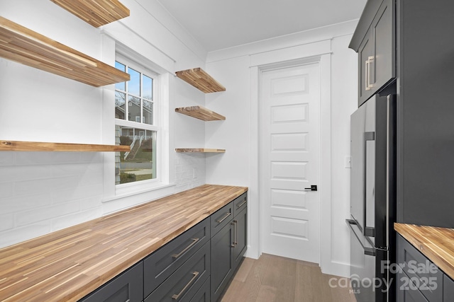 kitchen with butcher block counters, wood finished floors, backsplash, freestanding refrigerator, and open shelves