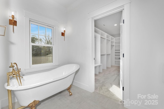 full bathroom with a soaking tub, a spacious closet, and baseboards